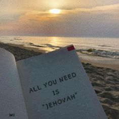 an open book sitting on top of a beach next to the ocean with a sunset in the background