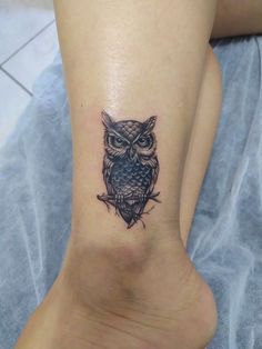 an owl tattoo on the foot of a woman's leg, which is black and grey