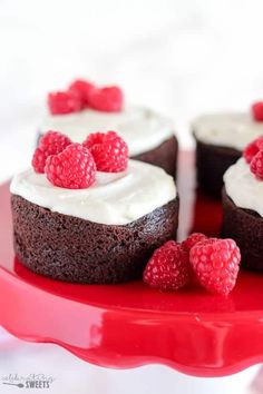 three chocolate cakes with white frosting and raspberries on a red platter