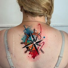 a woman's back with a compass tattoo on her left shoulder and colorful ink splatters all over it