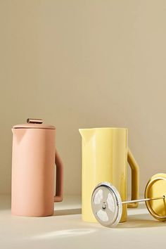 three different colored coffee mugs next to each other on a white surface with a yellow handle