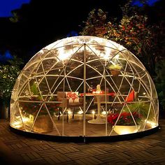 a glass dome with lights inside sitting on a brick patio in front of some trees