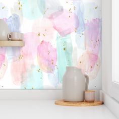 a white vase sitting on top of a counter next to a wall covered in watercolor paint