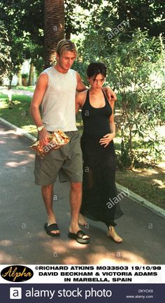 a young man and woman walking down the street in front of trees - stock image