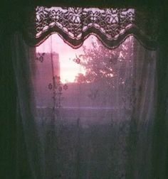 the sun is shining through the window in the dark room with sheer curtains on the windowsill