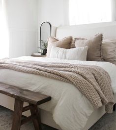 a bed with white linens and pillows in a small room next to a wooden bench