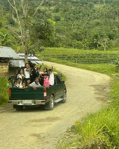 a group of people riding in the back of a pick up truck on a dirt road