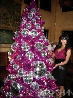 a woman standing in front of a purple christmas tree with disco balls on the top