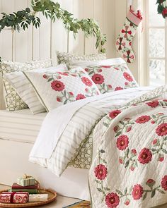 a white bed topped with lots of pillows and blankets next to a christmas wreath on top of a window sill