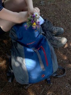 a person sitting on the ground with a blue backpack and flowers in their lap,