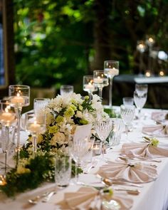 a long table is set with white and green floral centerpieces, gold candlesticks, and plates