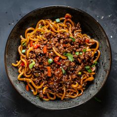 a bowl filled with noodles and meat on top of a black countertop next to chopsticks