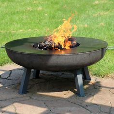 a fire pit sitting on top of a stone floor next to green grass and trees