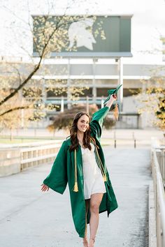 a woman is walking down the street wearing a green graduation robe and she has her arms in the air