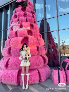 a woman standing in front of a pink christmas tree made out of fake furs