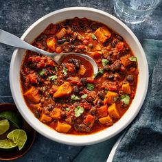 a white bowl filled with chili and beans next to two limes on the side