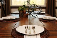 a wooden table topped with white plates and silverware