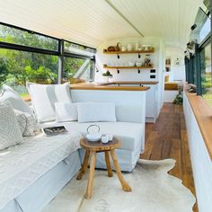 the inside of a tiny house with wood flooring and white couches, windows, and rugs