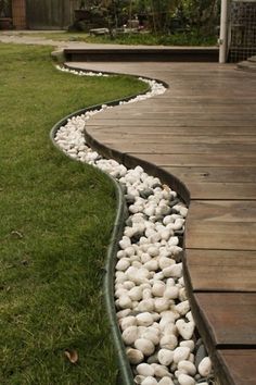 some rocks are laying on the ground in front of a wooden walkway that is lined with grass