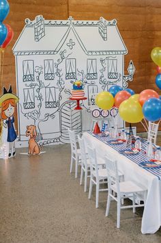 a table with balloons, cake and decorations on it in front of a drawing of a house