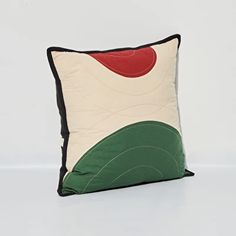 a white pillow with green and red designs on the front, sitting on a white surface