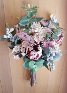 a bouquet of flowers sitting on top of a wooden table next to a wall with wood paneling