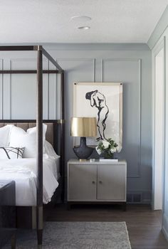 a white bed sitting next to a nightstand with a painting on it's wall