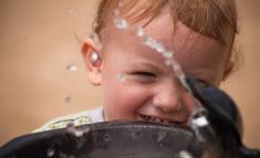 a little boy that is smiling and holding something in his hand with water coming out of it