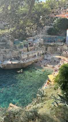 people are swimming in the clear blue water next to some cliffs and buildings on top of them