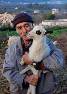 an old man holding a baby goat in his arms