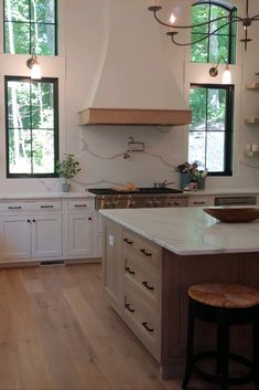 a large kitchen with white cabinets and wood flooring is pictured in this image, there are three windows above the sink