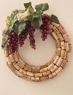 a wreath made out of wine corks with grapes on top and green leaves hanging from it