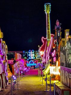 neon signs are lit up at night in an amusement park with people walking around them