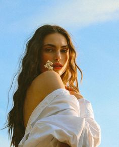 a woman with long hair wearing a white shirt and holding her hand on her hip