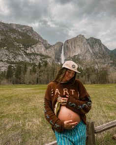 a pregnant woman is standing in front of a waterfall with her hands on her stomach