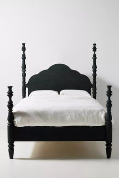 a black bed frame with white sheets and pillows on the headboard, against a white wall