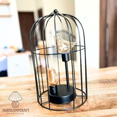 a bird in a cage on top of a wooden table next to a light bulb