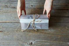 a person holding a wrapped present box on top of a wooden table with twine