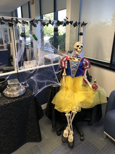 a skeleton dressed up in a yellow dress sitting on a chair next to a table