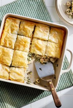 a casserole dish filled with meat and vegetables on a green place mat next to a spoon