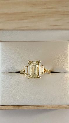 a yellow diamond ring sitting on top of a white leather case in a wooden box