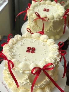 two white cakes with red ribbons and numbers on them