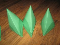 three green origami pieces sitting on top of a wooden floor next to each other