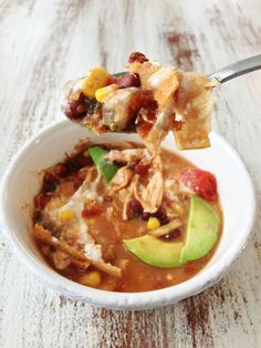 a white bowl filled with chicken tortilla soup and topped with avocado