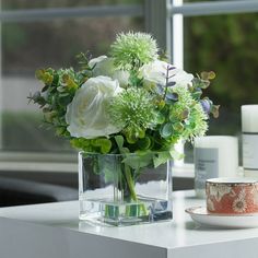 a vase filled with white flowers sitting on top of a table next to a cup and saucer