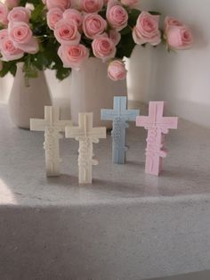 three small crosses are sitting on a table next to pink roses