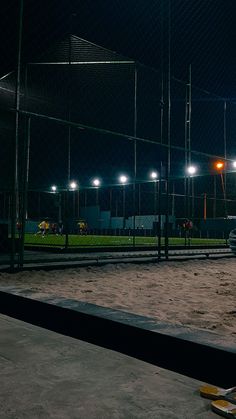 an empty baseball field at night with lights on and cars parked in the parking lot