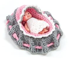 a baby doll in a crocheted basket with pink and gray trimmings