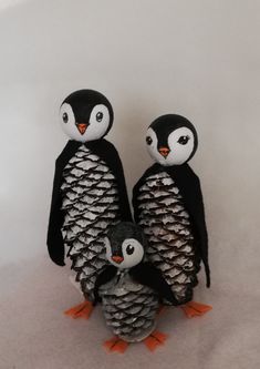 two penguins are standing next to each other with pine cones on their feet and one penguin is holding an egg in its beak