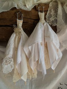 two dresses are hanging on a wooden hanger next to white lace and doily